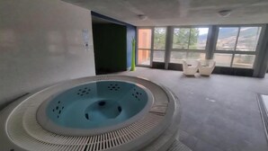 Un espace spa comprenant un bain à remous circulaire, un coin salon avec des fauteuils et de grandes fenêtres offrant une vue panoramique.