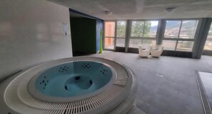 Ein Wellnessbereich mit einem runden Whirlpool, einer Sitzecke mit Sesseln und großen Fenstern mit Aussicht.