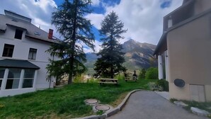 Un sentier menant à un bâtiment, avec une montagne en toile de fond, entouré de verdure et d’arbres.