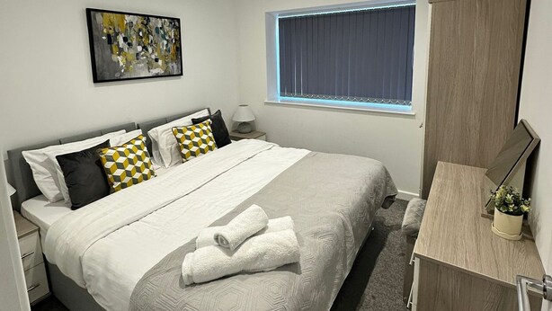 A modern bedroom with a bed, bedside table, window, and a painting on the wall. - Peaceful 2BR Stay with Fast Reliable Wi-Fi (Kingston upon Hull)