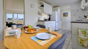 Un comedor con una mesa preparada para el desayuno, una cocina al fondo y vistas al exterior.