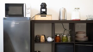 Una piccola angolo cottura completa di frigorifero, microonde, macchina del caffè e diversi utensili da cucina.