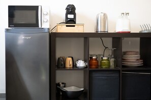 A compact kitchenette with a refrigerator, microwave, coffee maker, and various kitchenware. - GuestHost - Cozy Apartment Pigneto Metro C (Roma)