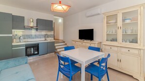 A modern kitchen with grey cabinets, a white dining table with blue chairs, a flat-screen TV, and a cabinet with glass doors. - Apartment 'Villino San Teodoro' with Private Terrace, Garden and Air Conditioning (San Teodoro)