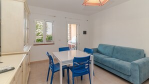 A room with a dining table, chairs, a sofa, and a ceiling light fixture. - Apartment 'Villino San Teodoro' with Private Terrace, Garden and Air Conditioning (San Teodoro)
