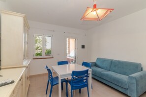 A room with a dining table, chairs, a sofa, and a ceiling light fixture. - Apartment 'Villino San Teodoro' with Private Terrace, Garden and Air Conditioning (San Teodoro)