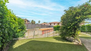 A well-maintained outdoor area with a grassy lawn, a fence, and a building with a tiled roof. - Private Luxury Room in Central San Teodoro with Private Terrace, Garden, and Air Conditioning (San Teodoro)