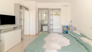 A bedroom with a bed, a TV, a wardrobe, a bathroom, and a small table with a lamp. - Private Luxury Room in Central San Teodoro with Private Terrace, Garden, and Air Conditioning (San Teodoro)