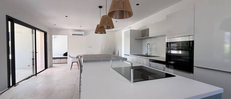 Een moderne keuken met een centraal eiland, een eethoek met een glazen tafel, en een grote schuifpui die leidt naar een balkon.