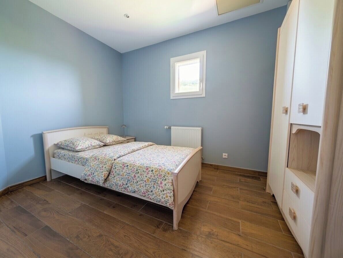 A bedroom with a bed, a radiator, a window, and a wardrobe.