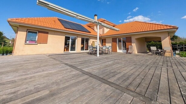 Ein Haus mit Holzterrasse, Solaranlage und einer Terrasse mit Gartenmöbeln.