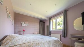 Ein Schlafzimmer mit einem Bett, einem Nachttisch, einem Spiegel, einem Fenster mit Vorhängen und einem an der Wand befestigten Regal.