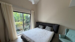 A bedroom with a bed, a window with curtains, a ceiling fan, and a light blue armchair. - Location La Balise (Black River)