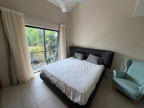 A bedroom with a bed, a window with curtains, a ceiling fan, and a light blue armchair. - Location La Balise (Black River)