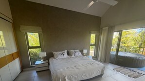 A bedroom with a large bed, two bedside tables with lamps, a view of the outdoors, and a hot tub. - Location La Balise (Black River)