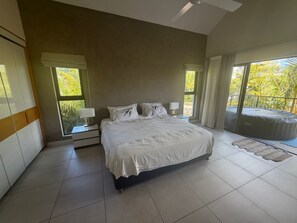 A bedroom with a large bed, two bedside tables with lamps, a view of the outdoors, and a hot tub. - Location La Balise (Black River)
