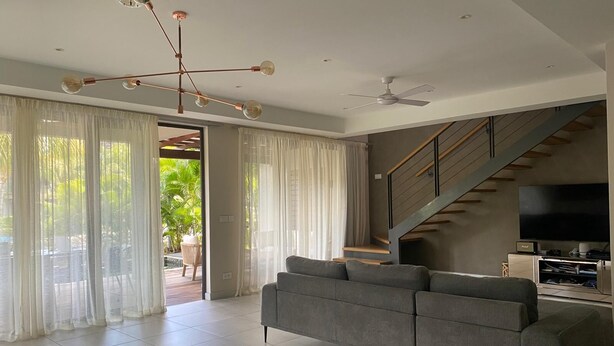 A modern living room with a sofa, a TV, a staircase, and a ceiling fan. - Location La Balise (Black River)
