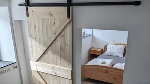 Una habitación con puerta corredera de madera, cama con cabecera de madera, mesita de noche y sofá gris.