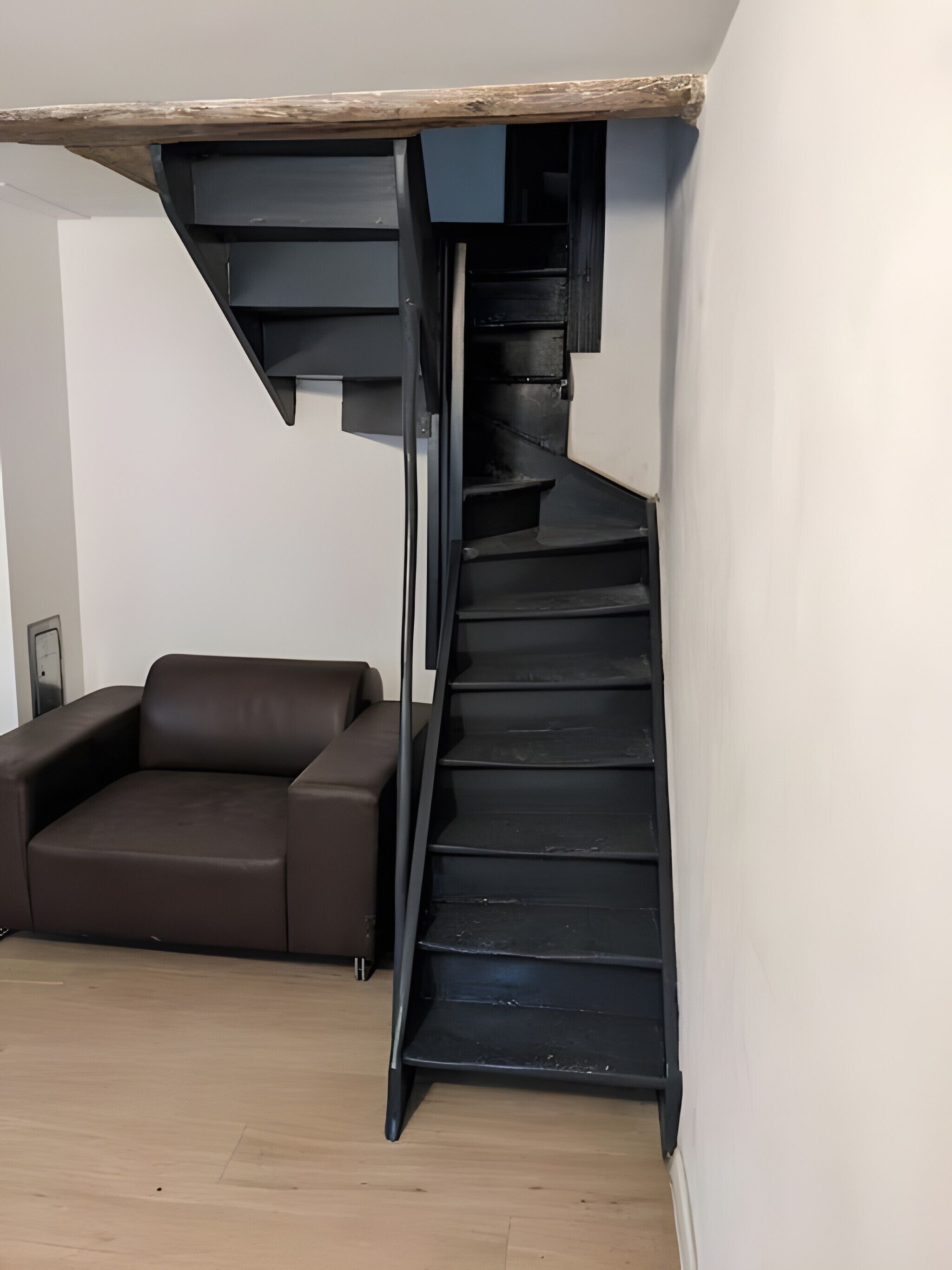 Un intérieur moderne avec un escalier en colimaçon noir, un canapé en cuir marron et une poutre en bois au plafond.