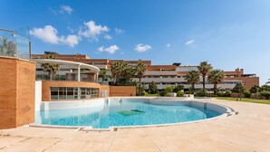 Una piscina de borde curvo, rodeada por un área empedrada y un edificio con balcones.