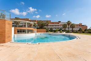 Una piscina de borde curvo, rodeada por un área empedrada y un edificio con balcones.