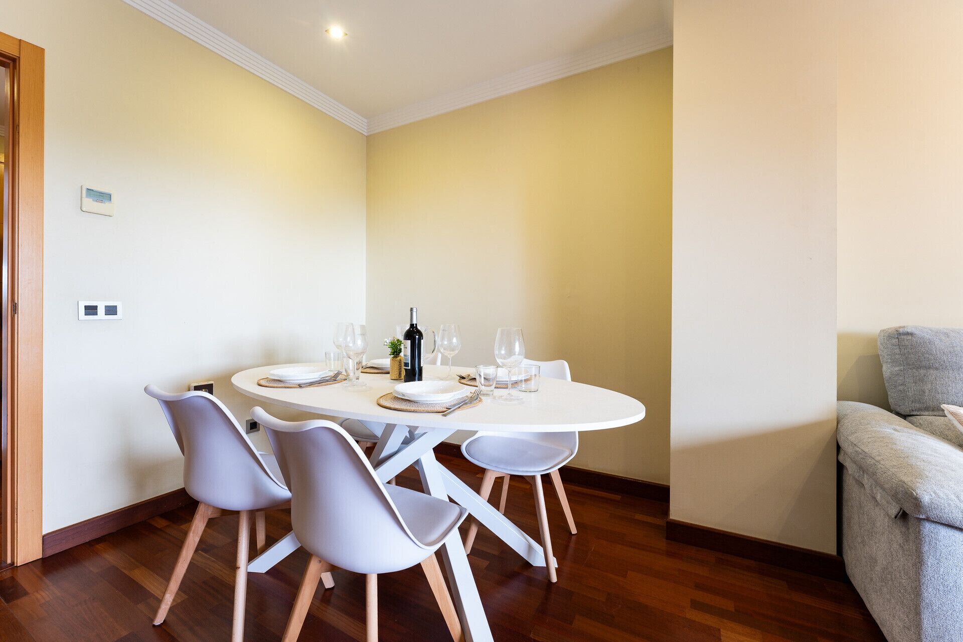 Uma área de refeições com uma mesa redonda, cadeiras brancas e uma garrafa de vinho.