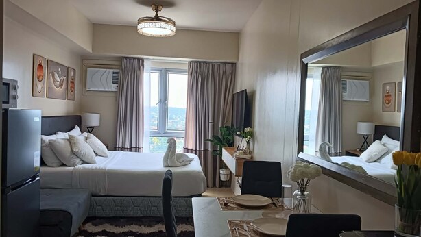 Ett hotellrum med en säng, ett skrivbord, en stol, en tv och en stor spegel.