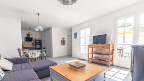 Una sala moderna con un sofá, una mesa de centro, un televisor y una cocina al fondo.