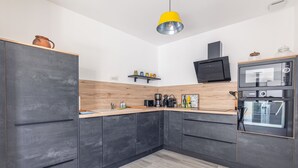 Una cocina moderna con armarios oscuros, encimera de madera, lámpara colgante amarilla, televisor negro y horno empotrado.