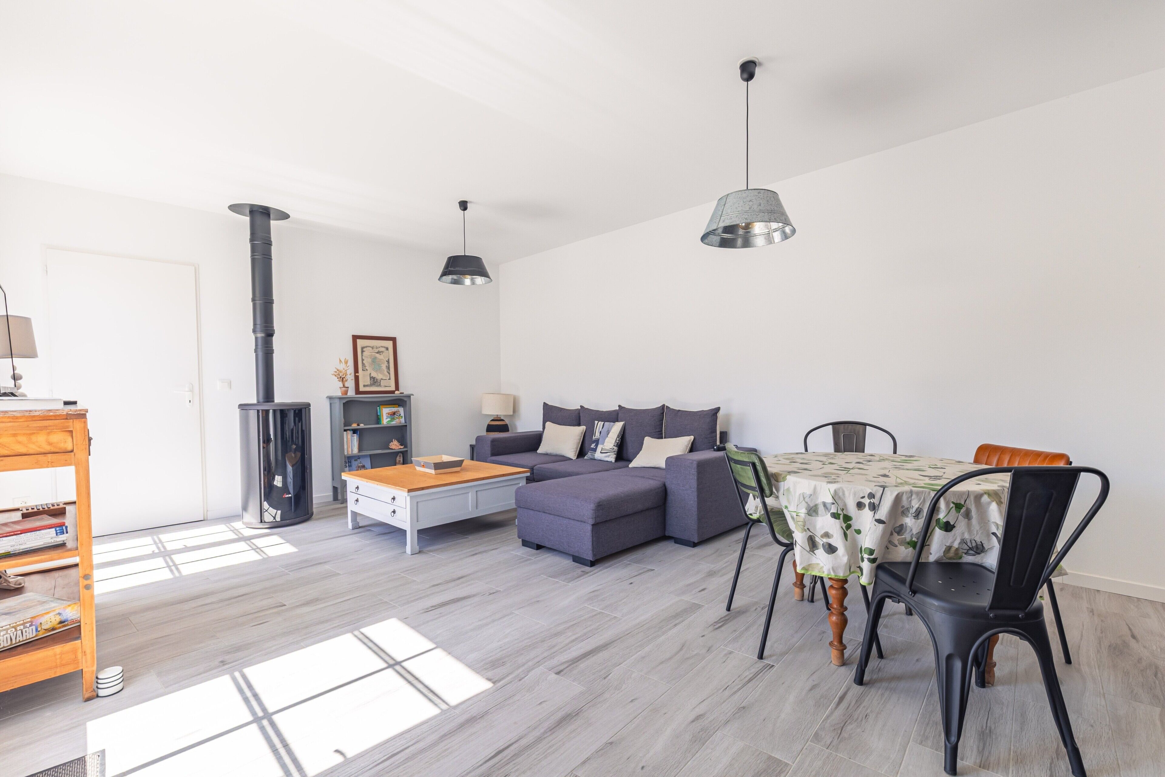 A modern living room with a sofa, dining table, and pendant lights.