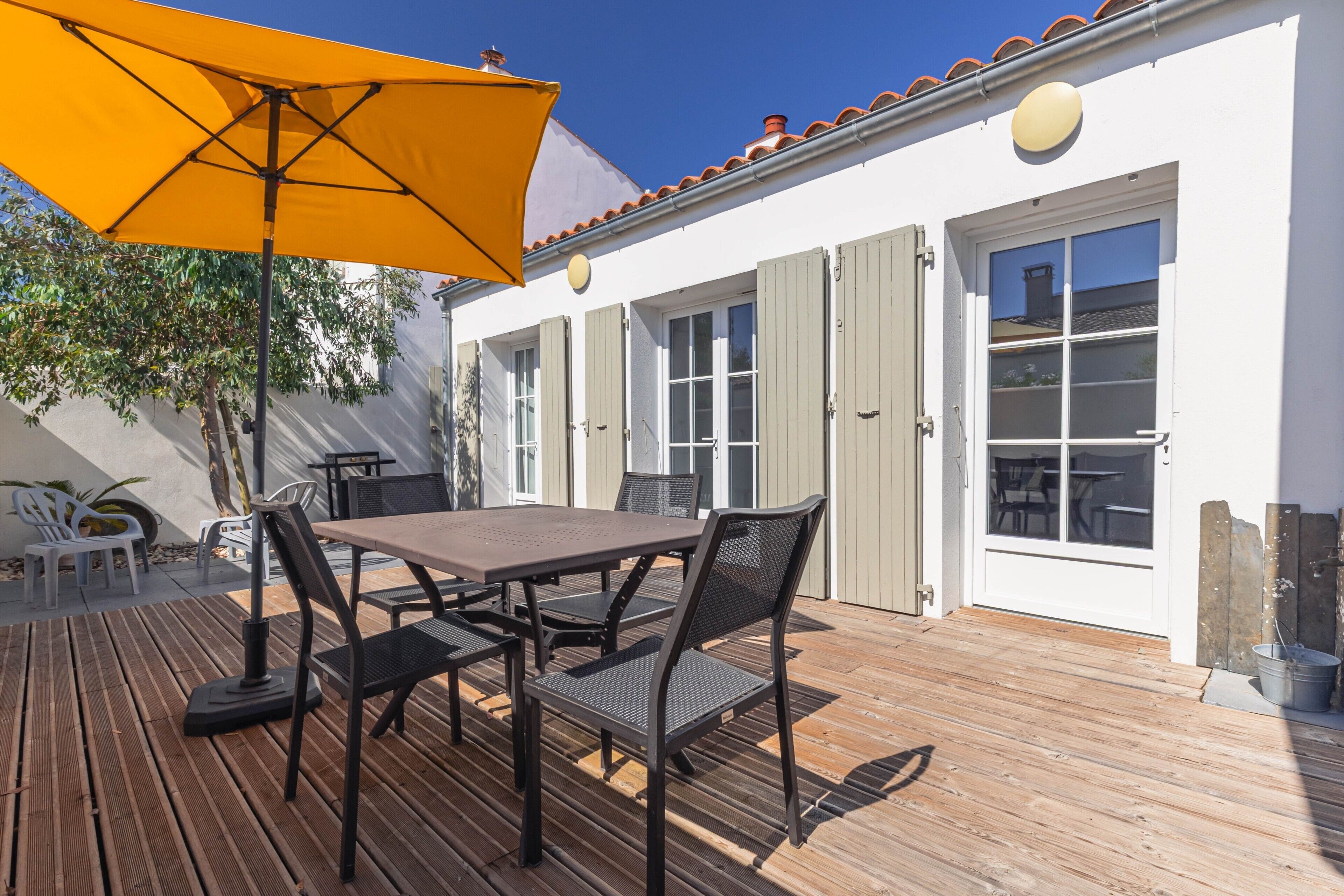Eine Terrasse im Freien mit Holzdeck, einem Tisch, Stühlen und einem gelben Sonnenschirm.