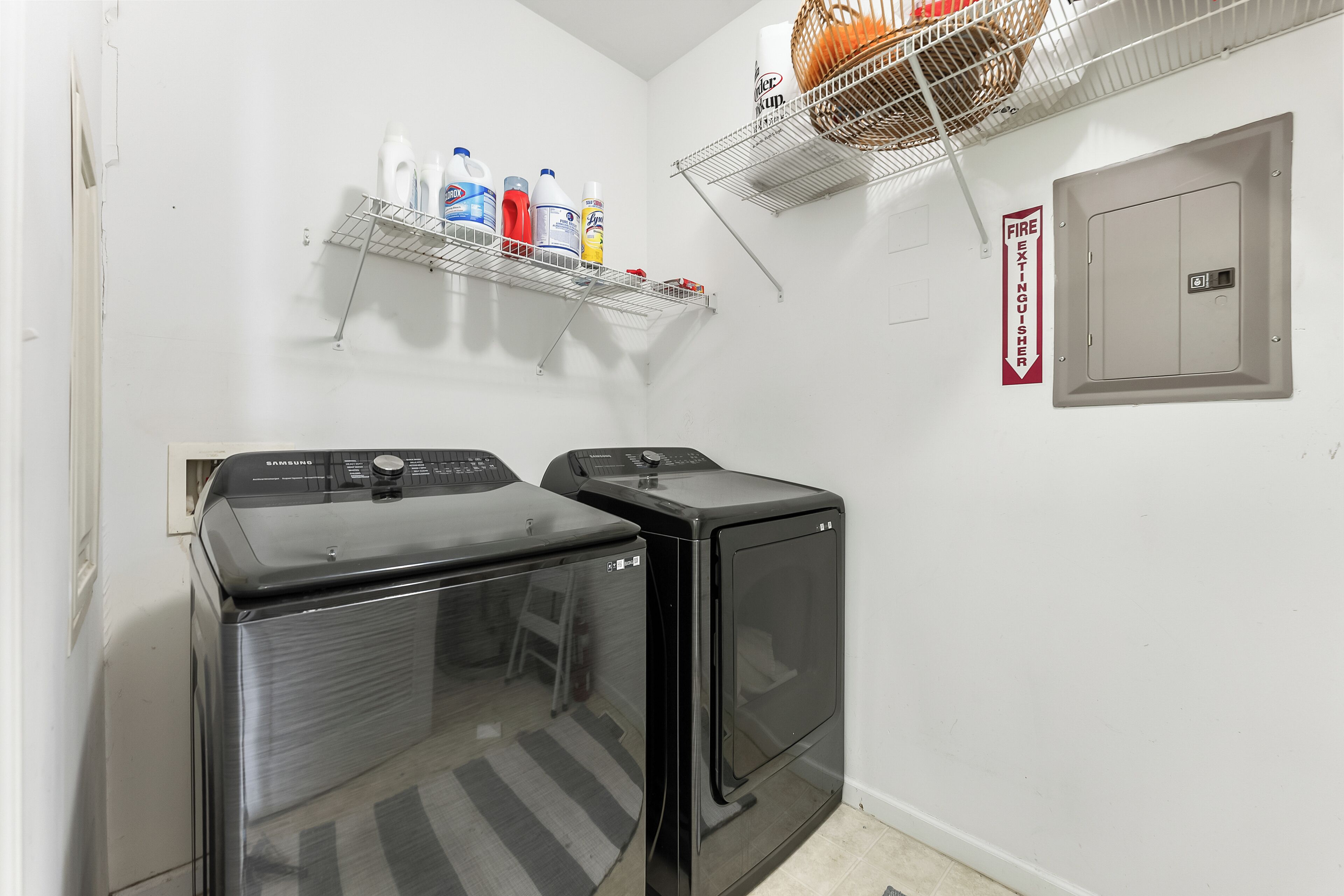 A laundry room with a Samsung washer and dryer, a fire extinguisher, and shelves with cleaning supplies.