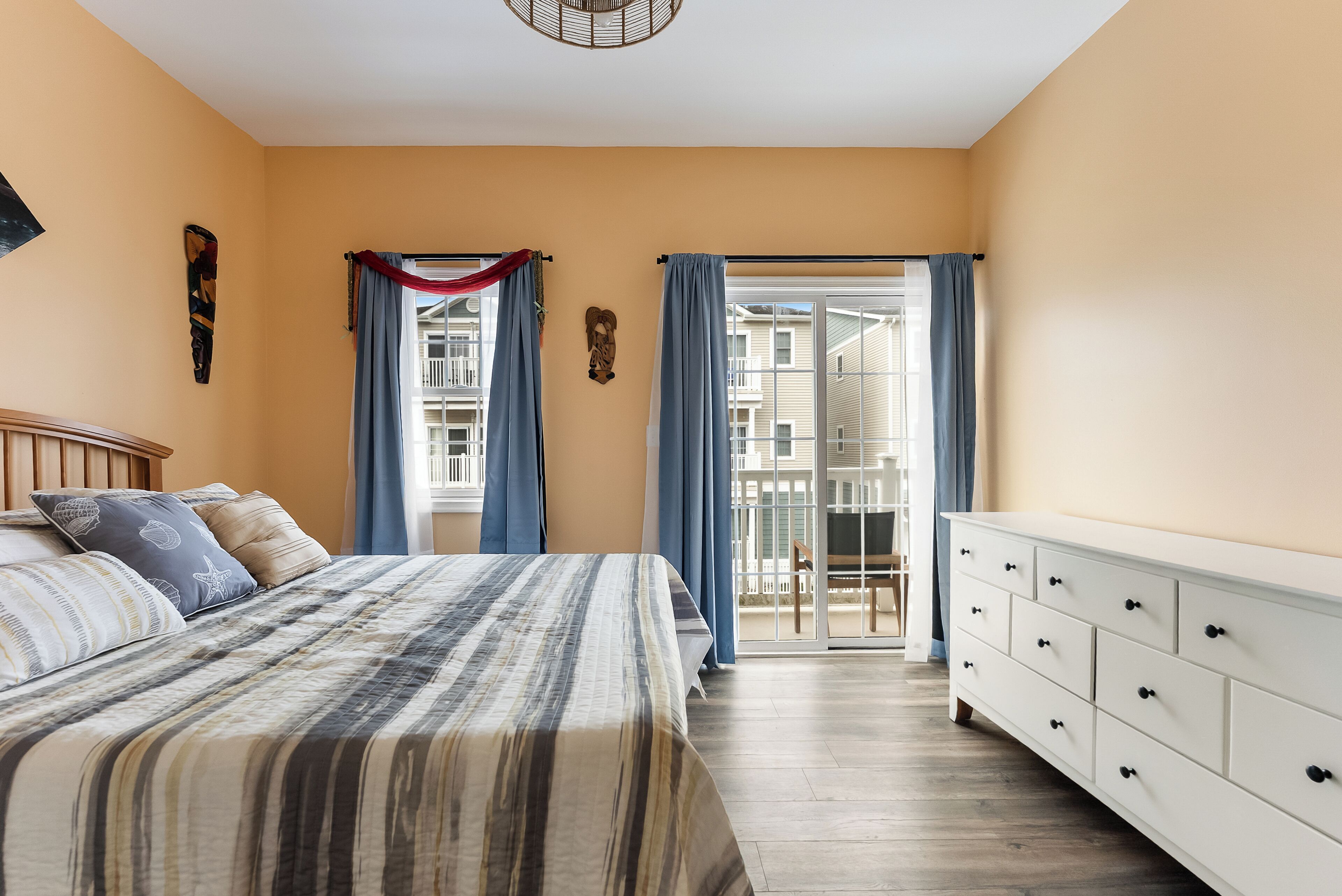 Ein Schlafzimmer mit Bett, Schminktisch, einem Fenster mit Vorhängen und einem Balkon.