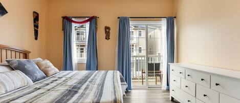Ein Schlafzimmer mit Bett, Schminktisch, einem Fenster mit Vorhängen und einem Balkon.
