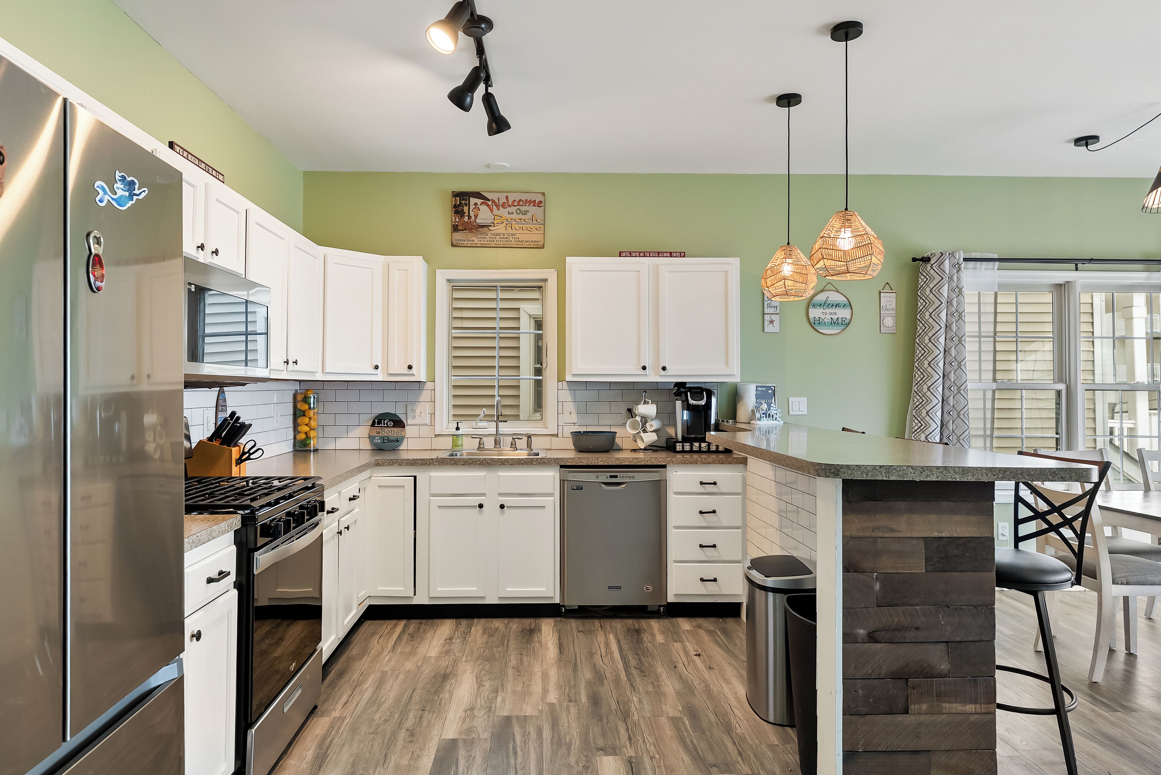 A kitchen with white cabinets, a stainless steel refrigerator, a dishwasher, and a built-in island with bar stools.