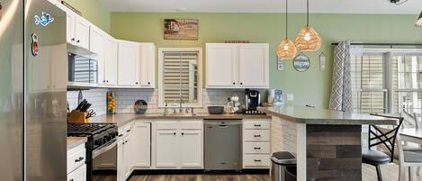 A kitchen with white cabinets, a stainless steel refrigerator, a dishwasher, and a built-in island with bar stools.