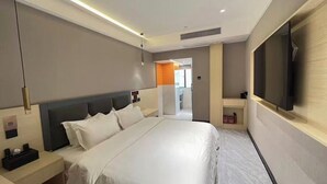 Habitación de hotel moderna con una cama grande, mesitas de noche, un televisor y un baño visible a través de una puerta abierta.