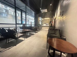 Ein modernes Interieur mit einem langen Korridor, einer Sitzecke mit Tischen und Stühlen sowie großen Fenstern mit Ausblick nach draußen.