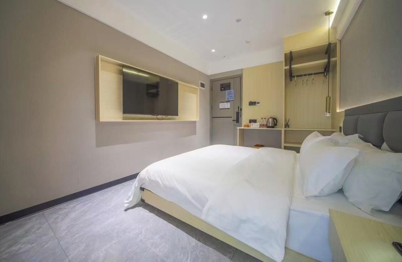 A modern hotel room with a large bed, a built-in TV, a wardrobe, and a small seating area.