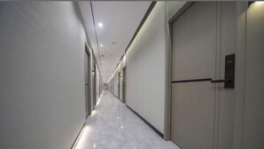 Un pasillo largo y estrecho con piso brillante, puertas a un lado y luces empotradas en el techo.