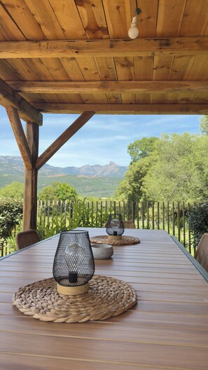 A wooden table with woven placemats and metal lanterns, set outdoors with a view of green hills and mountains. - Charming sheepfold, comfortable and ideally located (Figari)
