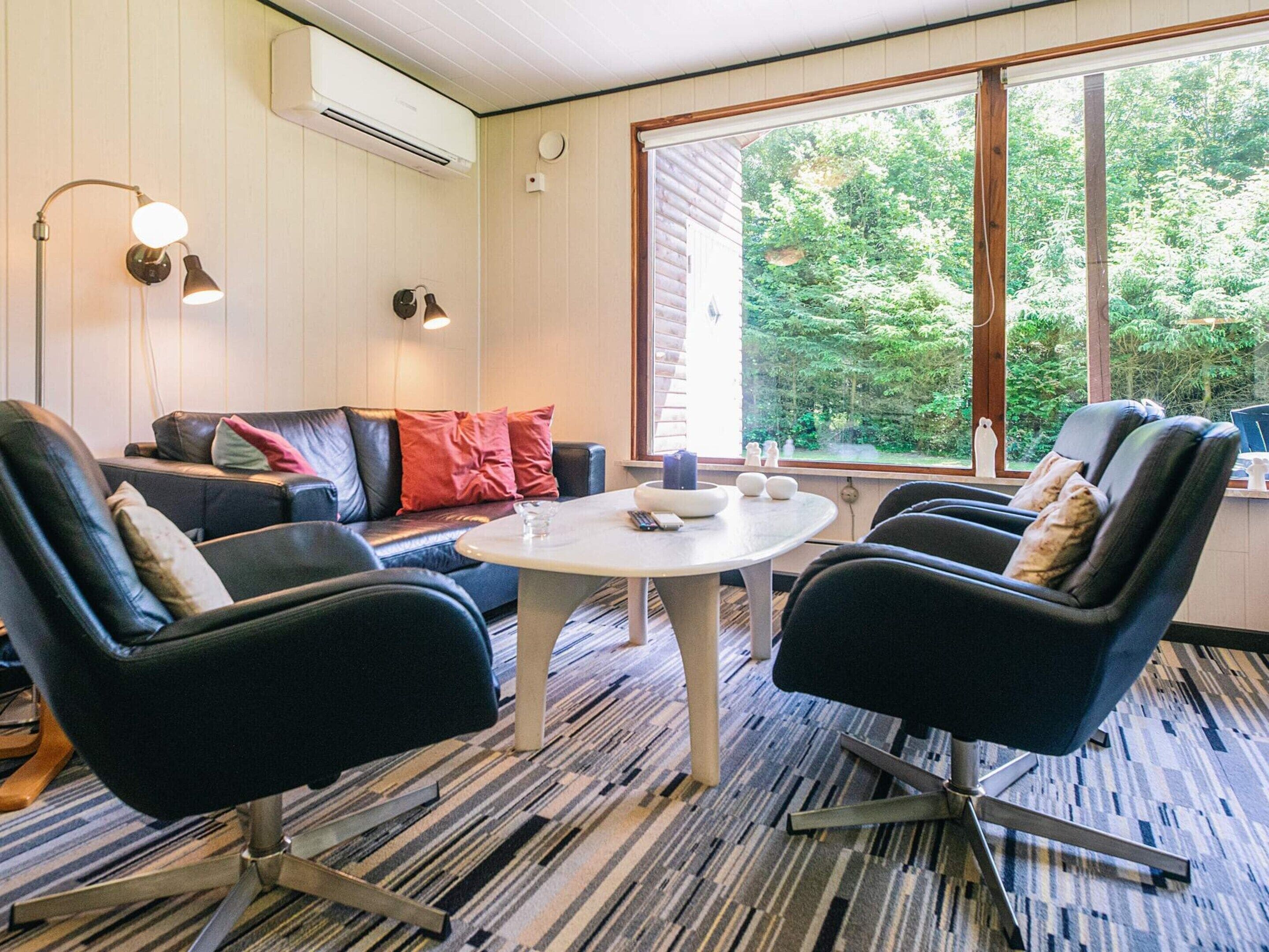 A room with a sofa, two chairs, a table, and a large window with a view of trees.