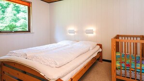 A bedroom with a wooden bed, a crib, a window with a view of greenery, and wall-mounted lights. - 6 Person Holiday Home in Hadsund (Hadsund)