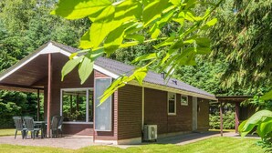 A single-story brick house with a covered patio, a small outdoor seating area, and a lawn. - 6 Person Holiday Home in Hadsund (Hadsund)