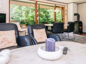 Ein modernes Wohnzimmer mit Ledersesseln, einem Marmortisch, einem Kamin und einem großen Fenster mit Blick auf Grünflächen.