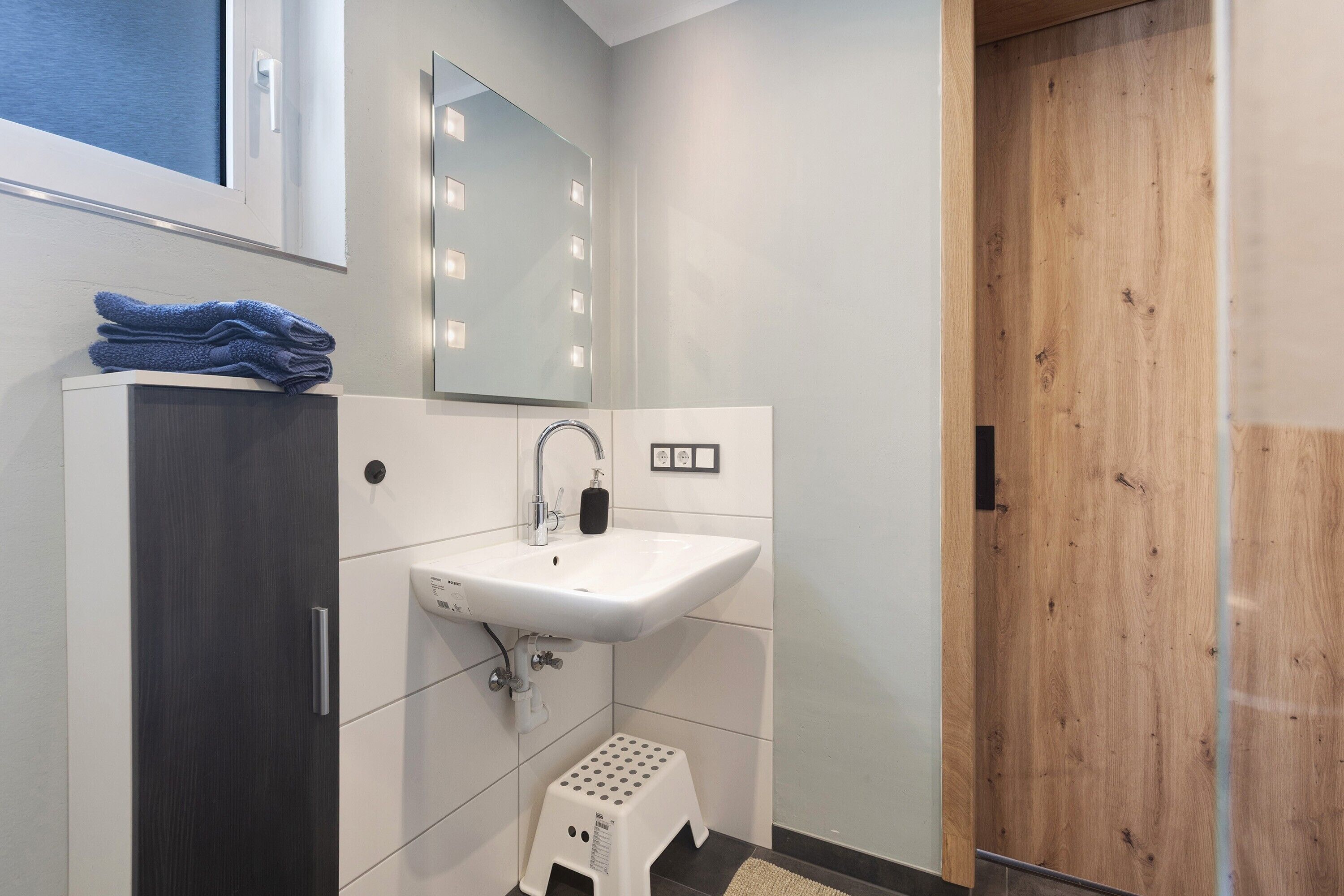 Ein modernes Badezimmer mit Waschbecken, Spiegel und Holztür.