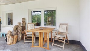 Una mesa de madera con sillas, troncos de árbol grandes y una ventana con vista a árboles.