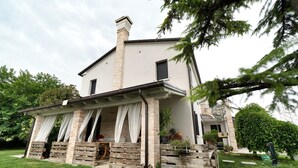 A two-story house with a covered porch, a chimney, and a well-maintained lawn. - Bed and Breakfast Al Vecio Morer 'Camera Rose' with Air Conditioning (San Donà di Piave)