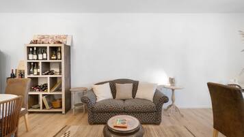 Een woonkamer met een gestreept sofa, een houten boekenkast, een ronde salontafel en een klein bijzettafeltje.