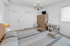 A bedroom with a bed, a desk, a chair, a wardrobe, and a chandelier.